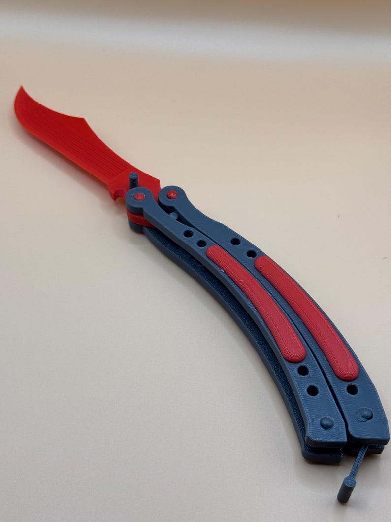 May include: A red and blue butterfly knife with a curved blade. The blade is open and the handle is closed.