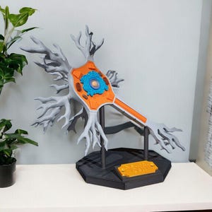 May include: A 3D-printed neuron model in grey, orange, and blue. It is mounted on a black hexagonal base with a gold plaque reading "Nerve Cell". The model depicts the structure of a nerve cell, including dendrites, a cell body, and an axon.