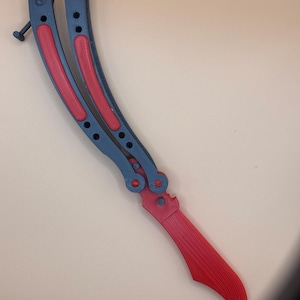 May include: A black and red butterfly knife with a curved blade. The handle is black with red accents.