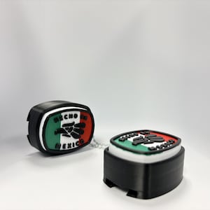 May include: Two black, square-shaped charms with rounded corners, featuring a raised design of the Mexican flag in green, white, and red. The text HECHO EN MEXICO is embossed in black lettering across the top and bottom of the flag emblem.