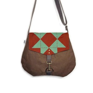 May include: A brown messenger bag with a geometric flap design. The flap features a pattern of red diamonds and green triangles. The bag has a gray strap and a metal clasp closure. The bag is designed to be worn over the shoulder.