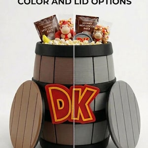Puede incluir: Un barril gigante con el texto "GIANT DK BARREL - NEW COLOR AND LID OPTIONS". El barril está dividido en secciones marrones y grises, con opciones de tapa a juego. El barril contiene snacks y juguetes de monos.