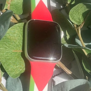 May include: A red, white, and green Apple Watch band with a black watch face. The band has a triangular design.