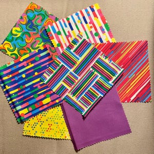 May include: A collection of colorful fabric swatches with various patterns. Designs include wavy lines, stripes, and polka dots in vibrant colors like blue, green, yellow, and red. One swatch is solid purple.