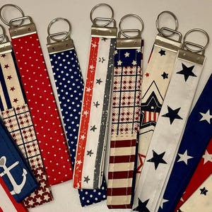 May include: A collection of patriotic-themed key fobs with various patterns. Designs include red and white stripes, blue with white stars, red polka dots, and a blue anchor design. Each fob has a silver-colored metal ring.