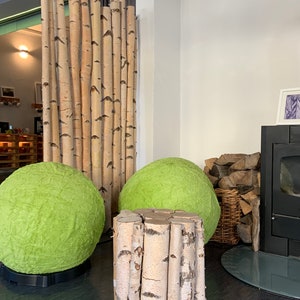 Könnte beinhalten: Zwei grüne Papierkugellampen und ein Hocker aus Birkenholz in einem Raum mit einem Birkenholz-Raumteiler und einem schwarzen Holzofen.