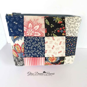 May include: A patchwork fabric zippered pouch with a variety of floral and geometric patterns in shades of blue, red, white, and black. The pouch has a gray zipper and the text "Glass Dreams Hawaii Lampwork Glass & Jewelry" is printed on the bottom.