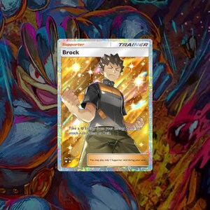May include: Brock, a Pokemon Trainer card from the Pokemon Trading Card Game. The card features a colorful illustration of Brock, a character from the Pokemon anime series. The card text reads "Take a  Energy from your Bench and attach it to Golem or Onix. You may play only 1 Supporter card during your turn."
