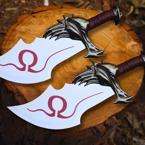 May include: Two fantasy-style blades with white blades and burgundy handles rest on a wooden surface. The blades have a stylized red Omega symbol. The handles are dark burgundy with silver-colored metal guards.
