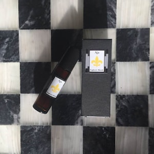May include: A black roll-on bottle of perfume with a white label that says "Aja Euphoric Blends". The bottle is sitting on a black and white checkered surface. A black box with a white label that says "Aja Euphoric Blends" is sitting on the checkered surface.