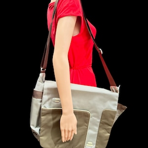 Könnte beinhalten: Eine braune und graue Umhängetasche mit einem langen verstellbaren Riemen. Die Tasche hat ein großes Hauptfach und eine kleinere Tasche vorne.