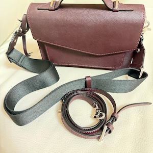 May include: A burgundy handbag with a top handle and a detachable shoulder strap. The bag has a flap closure and silver-tone hardware. A second, thinner burgundy strap is also included.