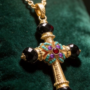 May include: A gold-toned cross pendant on a matching chain, featuring four large, faceted black beads at the ends. The center is decorated with a small red stone, four purple stones, and small turquoise-colored accents in a floral pattern.