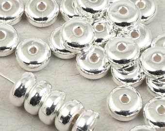 May include: A large quantity of silver-toned metal spacer beads. The beads are round with a hole in the center. The beads are arranged in a pile on a white surface.