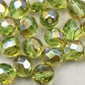 May include: A collection of green glass beads with iridescent facets. The beads are round and have a faceted design.