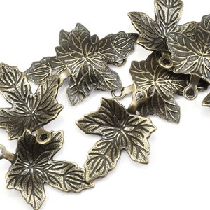May include: A set of eight antique gold-toned metal leaf charms. Each charm features a detailed, textured design of a maple leaf.