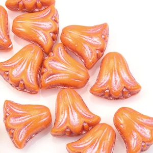 May include: A collection of orange glass flower-shaped beads with a pearlescent finish. The beads are scattered on a white surface.