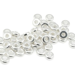 May include: A pile of silver-toned metal spacer beads. The beads are round with a hole in the center. They are perfect for adding a touch of elegance to jewelry projects.