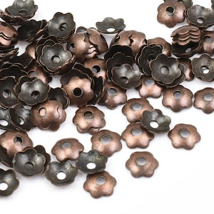 May include: A large pile of antique copper-toned metal flower-shaped bead caps. The caps have a small hole in the center and are designed to be used for jewelry making.