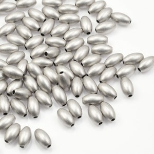 May include: A large pile of silver oval beads. The beads are smooth and have a matte finish.