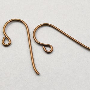 May include: Two copper-colored earring hooks are displayed against a light background. Each hook has a curved design with a looped end for securing to the ear and a straight wire portion.