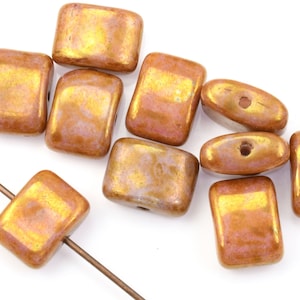 May include: A collection of rectangular and oval-shaped beads in shades of bronze and gold. The beads have a glossy finish and appear to be made of glass or a similar material. Some beads are strung on a thin wire, suggesting they are for jewelry making.