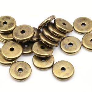 May include: A group of 14 gold-toned metal beads, each with a round hole in the center. The beads are scattered on a white surface.
