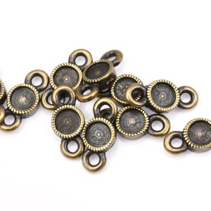 May include: A group of antique gold-toned metal bezel settings with two loops on each side. The bezels are designed to hold a round cabochon stone.