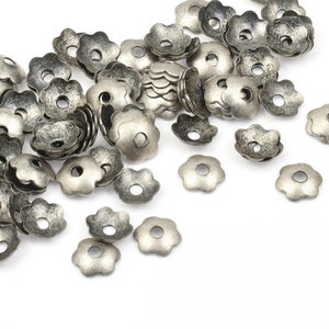 May include: A large quantity of silver-toned metal flower-shaped bead caps. The caps have a slightly distressed finish and are perfect for adding a touch of vintage charm to jewelry projects.