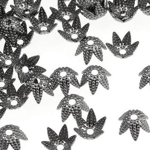 May include: A collection of dark gray, flower-shaped bead caps with a textured surface and a central hole. These metal components are scattered against a white background, ideal for jewelry making and crafting projects.