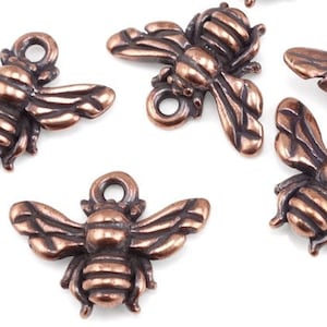 May include: Six copper-colored bee charms with detailed wings and bodies. The charms have a loop at the top for attaching to jewelry or other crafts.