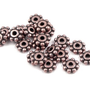 May include: A group of 14 copper-coloured metal bead caps with a decorative flower design. The bead caps are arranged in a loose pile on a white background.