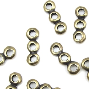 May include: A group of antique gold metal connector charms with three round holes each. The charms are scattered on a white surface.