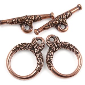 May include: Two copper-toned metal clasps with a butterfly and floral design. Each clasp has a ring and a hook.