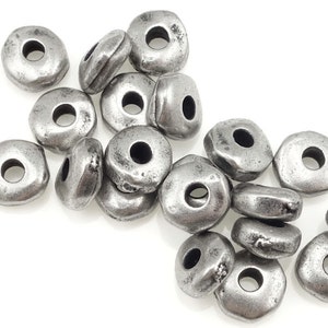 May include: A collection of silver-colored, irregularly shaped beads with a central hole. The beads have a rustic, weathered appearance, suggesting an antique or vintage style. These beads are suitable for jewelry making and crafting projects.
