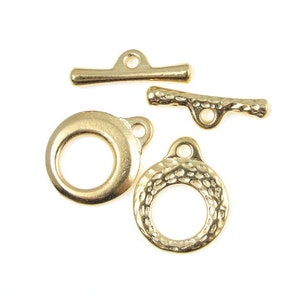 May include: Four gold-toned metal clasps for jewelry making. Two are round with a hole at the top, one is a straight bar with a loop at each end, and the other is a curved bar with a loop at each end.