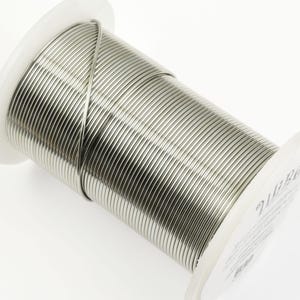 May include: A spool of silver-colored wire, wound tightly around a white plastic spool. The wire is smooth and shiny.