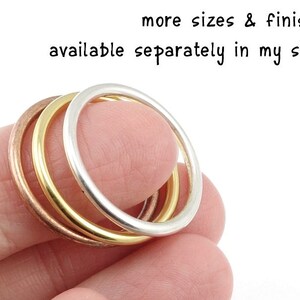 May include: Three stacked rings, one silver, one gold, and one copper. The rings are worn on a finger.