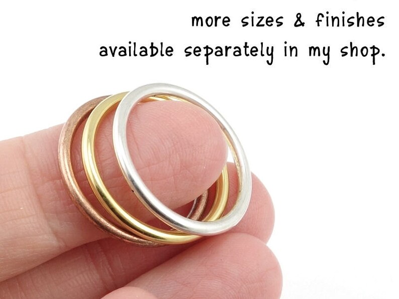 May include: Three stacked rings, one silver, one gold, and one copper. The rings are worn on a finger.