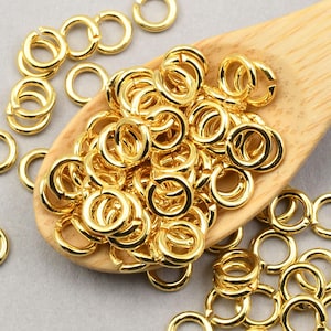 May include: A large pile of gold jump rings on a wooden spoon. The jump rings are small and round, and they are perfect for jewelry making.