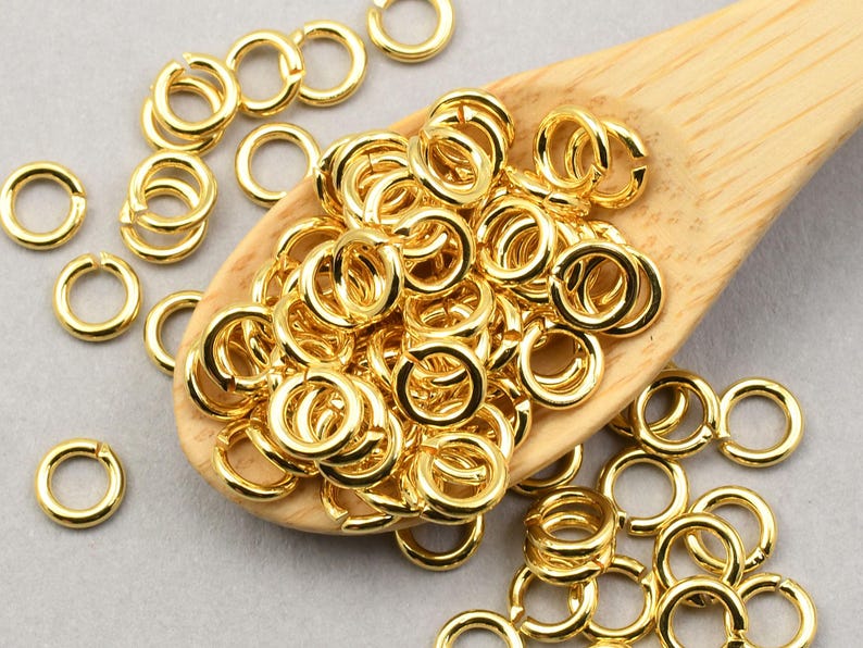 May include: A large pile of gold jump rings on a wooden spoon. The jump rings are small and round, and they are perfect for jewelry making.