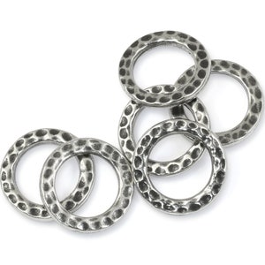 May include: A collection of six silver-colored, hammered-texture metal rings. The rings are circular with a slightly irregular surface, creating a textured appearance. They are arranged on a white background.