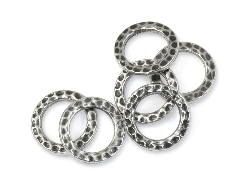May include: A collection of six silver-colored, hammered-texture metal rings. The rings are circular with a slightly irregular surface, creating a textured appearance. They are arranged on a white background.