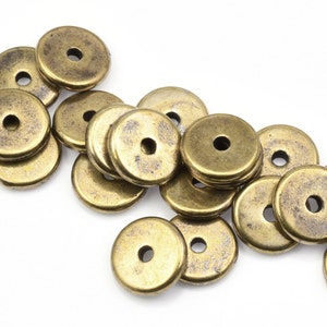 May include: A pile of antique gold-toned metal spacer beads. The beads are round with a hole in the center. They are perfect for jewelry making.