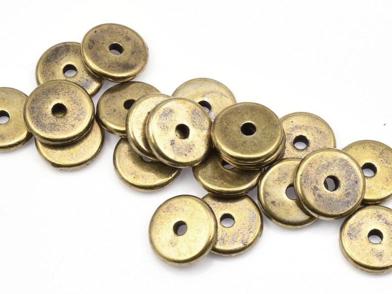 May include: A pile of antique gold-toned metal spacer beads. The beads are round with a hole in the center. They are perfect for jewelry making.