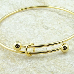 May include: A gold-colored adjustable bangle bracelet. The bracelet features two small, round gold beads on either end of the adjustable portion. The adjustable section has a looped design in the center.