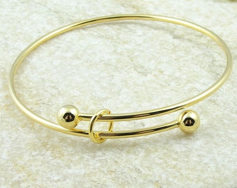 May include: A gold-colored adjustable bangle bracelet. The bracelet features two small, round gold beads on either end of the adjustable portion. The adjustable section has a looped design in the center.
