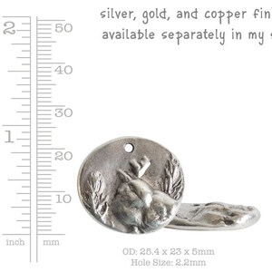 May include: Silver-toned metal charm featuring a detailed deer head design with a hole for attaching to a necklace or bracelet. The charm measures 25.4 mm in diameter, 23 mm in width, and 5 mm in thickness. The hole size is 2.2 mm.  The charm is available in silver, gold, and copper finishes.