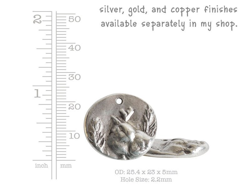 May include: Silver-toned metal charm featuring a detailed deer head design with a hole for attaching to a necklace or bracelet. The charm measures 25.4 mm in diameter, 23 mm in width, and 5 mm in thickness. The hole size is 2.2 mm.  The charm is available in silver, gold, and copper finishes.
