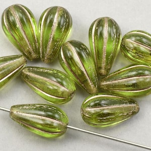 May include: A group of green glass beads with gold accents. The beads are teardrop shaped and have a textured surface.